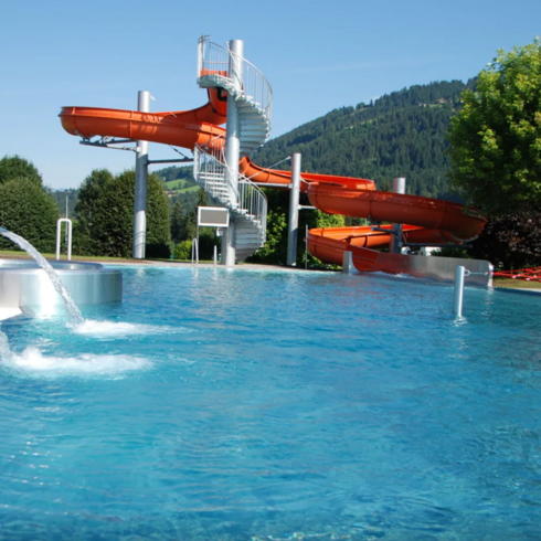 Ein entspannender Poolbereich mit einer Wasserrutsche und sprudelndem Wasser, umgeben von einer malerischen Berglandschaft.