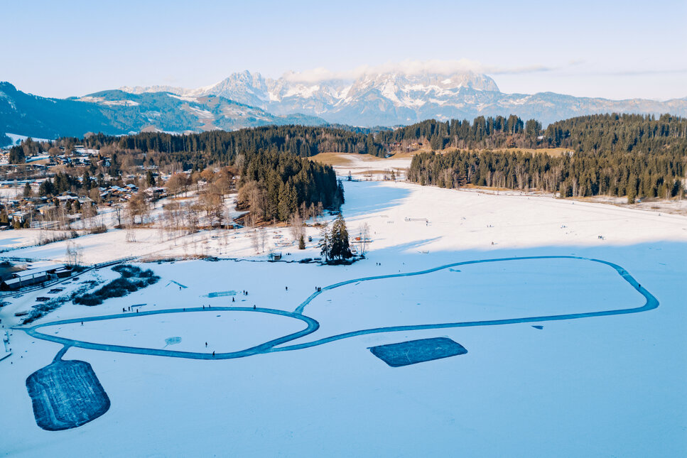 Luftaufnahme des gefrorenen Schwarzsees in Kitzbühel, auf dem Menschen Schlittschuh laufen und über das Eis spazieren.