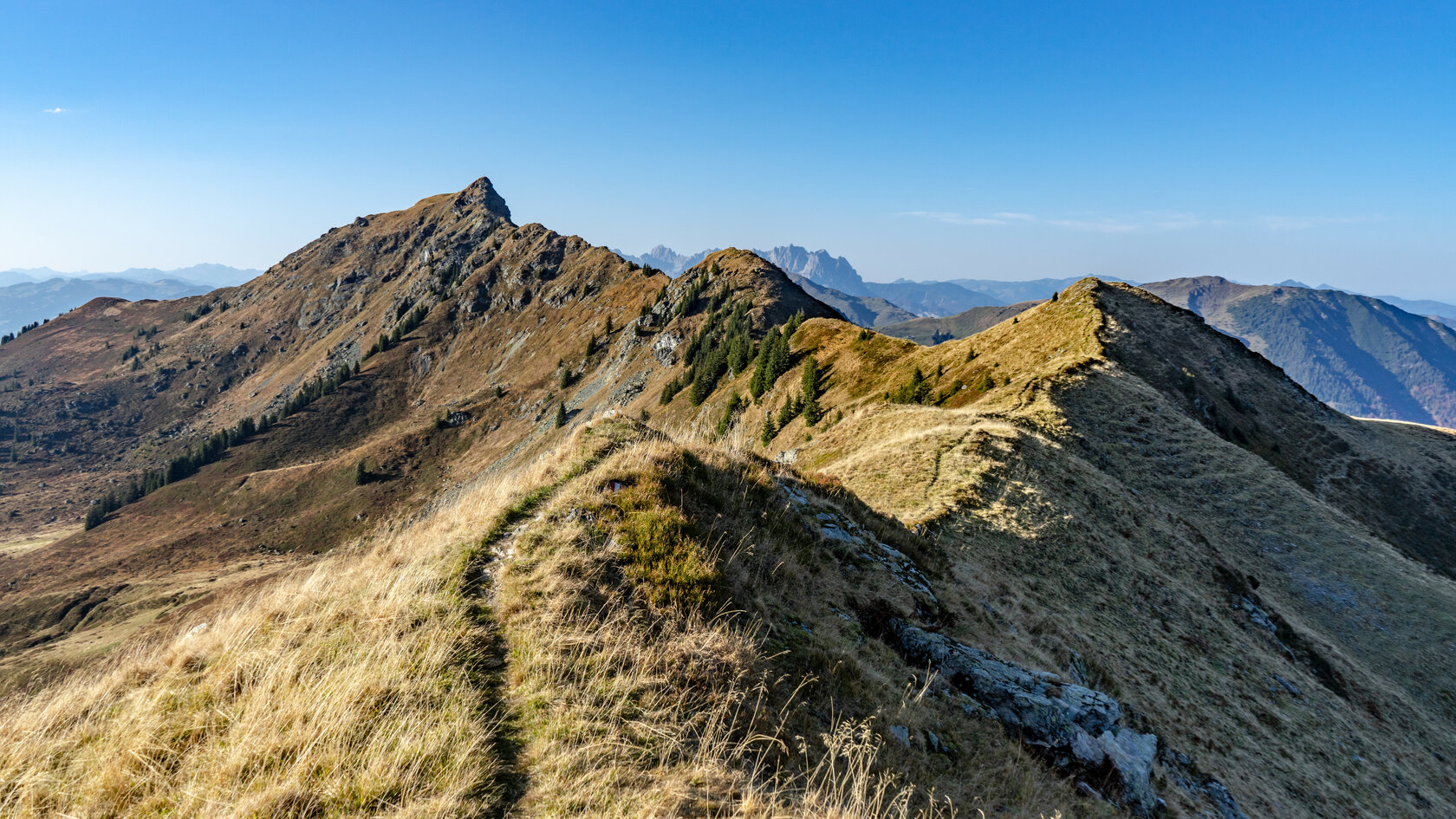 Die goldenen Gräser der Hügel kontrastieren mit den schroffen Felsen und den grünen Nadelbäumen in dieser malerischen Bergregion.