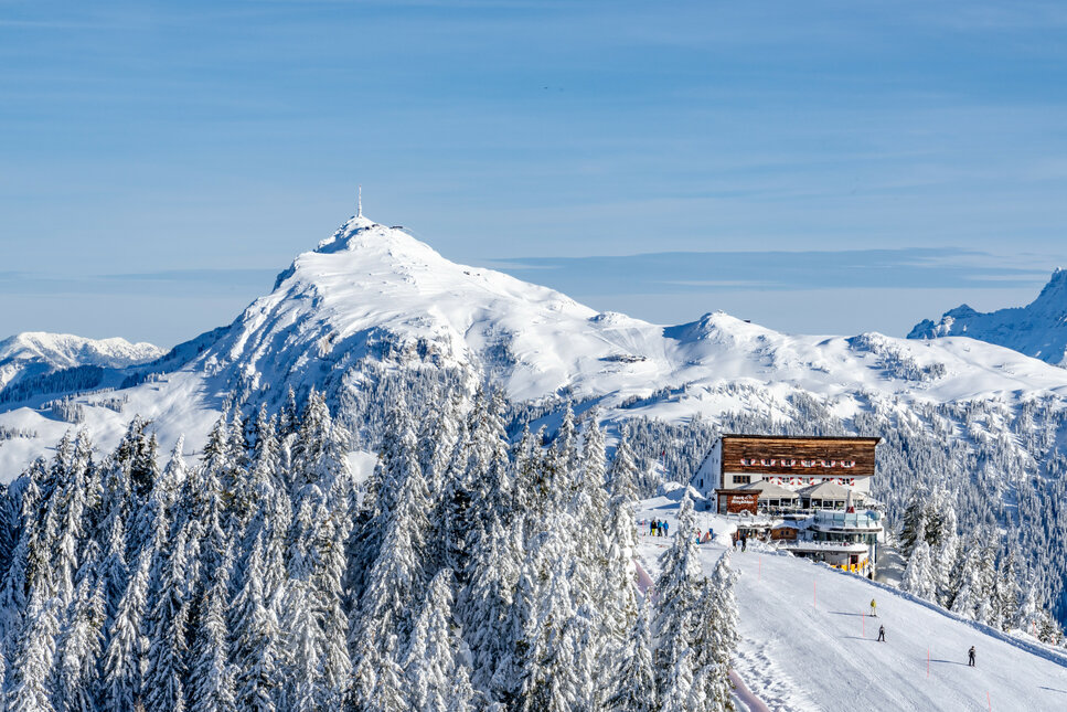 Hahnenkamm, Skigebiet Kitzbühel – Verschneite Berglandschaft mit einer Skihütte im Vordergrund und Gipfeln im Hintergrund.