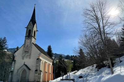 Kapelle in Kochau Kleine Kapelle mit spitzem Turm in einer verschneiten Winterlandschaft unter blauem Himmel.