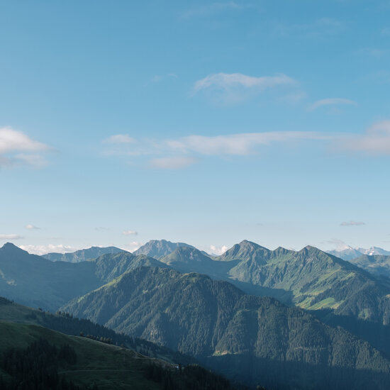 LH Südberge Eine atemberaubende Berglandschaft mit sanften Hügeln und schneebedeckten Gipfeln unter einem klaren blauen Himmel.