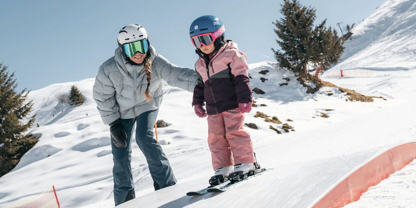 Family Snowpark Horn, Skigebiet Kitzbühel – Eine Mutter hilft ihrer Tochter beim Skifahren in verschneiter Umgebung.