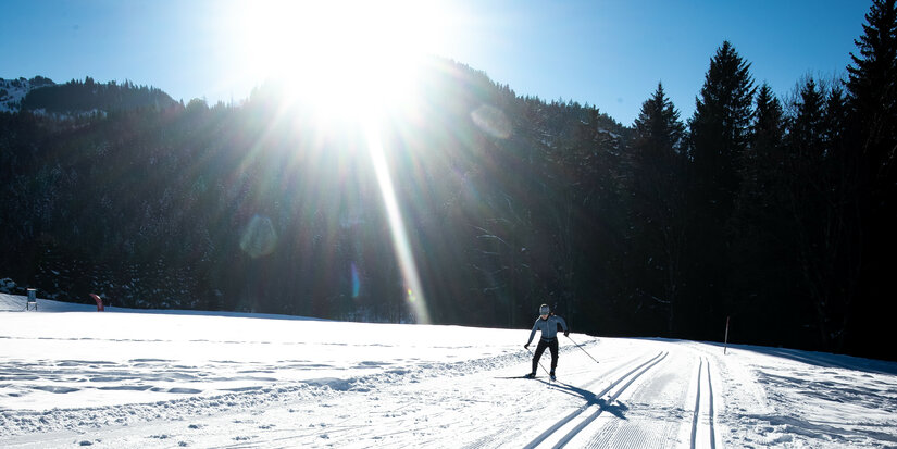 Beim Langlauf in Kitzbühel gleitet ein Langläufer über verschneite Fläche im hellen Sonnenlicht.