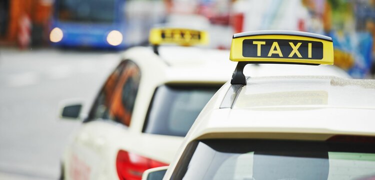 Zwei Taxis stehen an einer Straßenecke, während ein blauer Bus im Hintergrund vorbeifährt, was eine belebte Stadtatmosphäre schafft.
