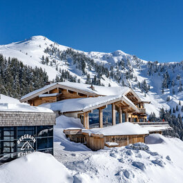 Berggasthof Bichlalm, Skigebiet Kitzbühel, in verschneiter Landschaft mit Tannen und Bergblick.