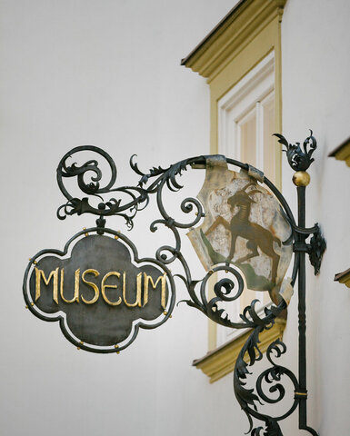 Ein historisches Schild mit dem Wort 'Museum', verziert mit filigranen Eisenarbeiten und einem abgebildeten Tier im Hintergrund.