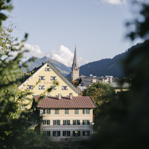 Kitzbühel mit bunten Häusern und Kirche, umgeben von Bergen und klarem Himmel.