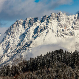 Blick von Kitzbühel auf den Wilden Kaiser mit schneebedeckten Gipfeln unter blauem Himmel.
