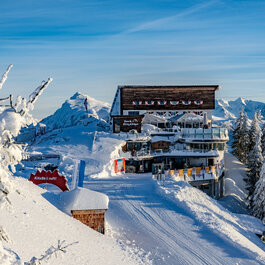 Bergstation Hahnenkammbahn, Skigebiet Kitzbühel, modernes Gebäude in verschneiter Berglandschaft mit Tannen.