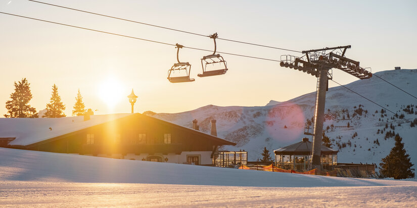 Sonnenrast Sessellift über verschneiter Piste im Morgenlicht, Skigebiet Kitzbühel.