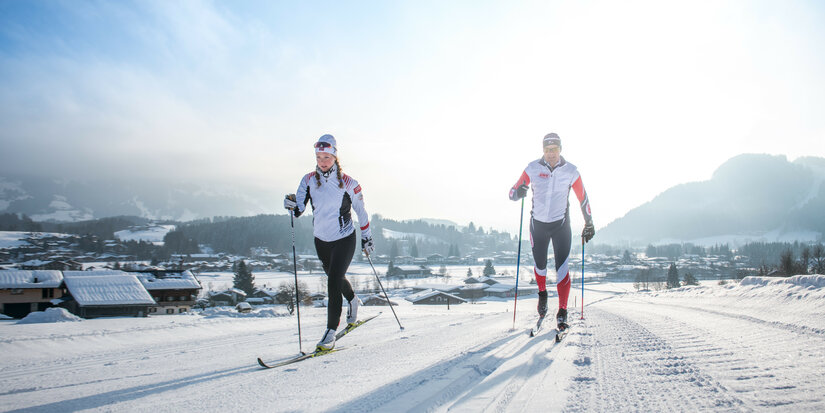 Zwei Langläufer gleiten über eine schneebedeckte Strecke, umgeben von einer malerischen Winterlandschaft in Kitzbühel.