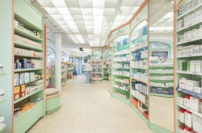 A bright pharmacy with shelves full of products. In the middle stands a person who is busy with the offered items.
