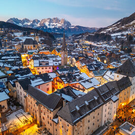 Blick auf die historische Altstadt von Kitzbühel, wo bunte Lichter und schneebedeckte Dächer eine zauberhafte Stimmung erzeugen.