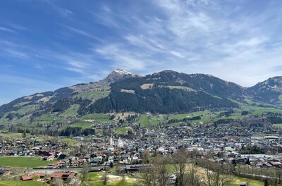 Blick auf eine Ortschaft im Tal vor bewaldeten Bergen unter blauem Himmel.