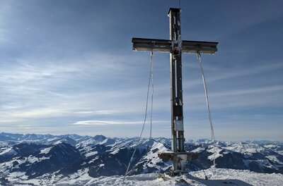 Gipfelkreuz an der Bichlalm Ein hölzernes Gipfelkreuz auf einem schneebedeckten Berg vor einem Panorama aus verschneiten Alpengipfeln.