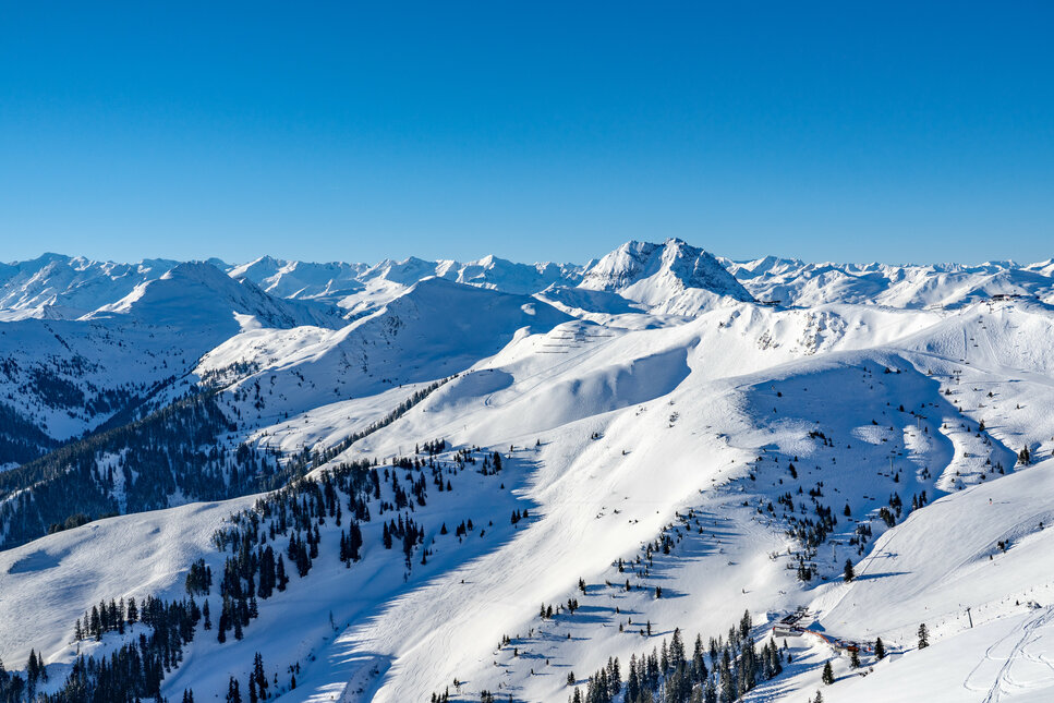 Steinbergkogel, Skigebiet Kitzbühel, Blick über verschneite Berglandschaft unter klarem, blauem Himmel.