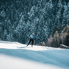 Beim Langlauf in Kitzbühel gleitet ein Langläufer elegant über verschneite Loipe vor Tannen im Hintergrund.