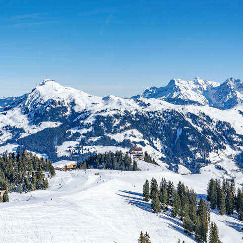 Eine atemberaubende Winterlandschaft mit schneebedeckten Bergen und einem klaren blauen Himmel über dem Skigebiet Hahnenkamm.
