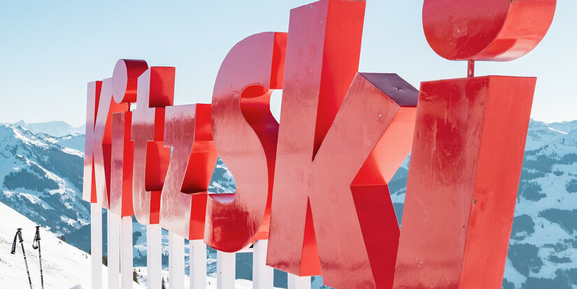 Steinbergkogel, Skigebiet Kitzbühel, rotes KitzSki Schild im Schnee vor Bergkulisse.