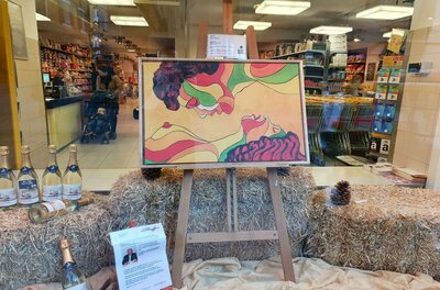 Billa Künstlerfenster Ein buntes Kunstwerk in einem Schaufenster, das zwei Profilgesichter zeigt. Darunter stehen Flaschen und dekoratives Stroh.