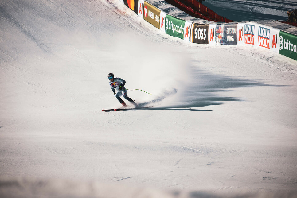 Zielbereich der Streif, Skigebiet Kitzbühel, Rennläufer in voller Fahrt auf der Piste mit aufspritzendem Schnee.