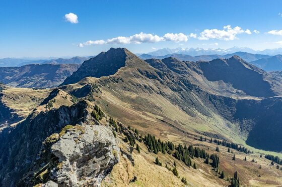 Gebra Bergpanorama im Herbst Blick auf einen grasbewachsenen Gebirgskamm mit felsigen Gipfeln unter blauem Himmel.