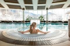<p>The spa area of the Grand Tirolia Kitzbühel features a large pool with a view of the Kitzbühel mountains. A woman sits at the edge of the pool, enjoying the peaceful atmosphere.</p>