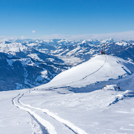 In den Südbergen im Skigebiet Kitzbühel steht ein Skitourengeher auf einem verschneiten Gipfel und blickt über die umliegenden Berge.