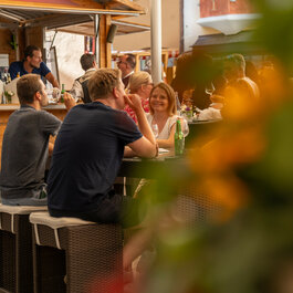 Eine Gruppe von Menschen sitzt im Freien beim Kulinarik-Festival in Kitzbühel und genießt Getränke.