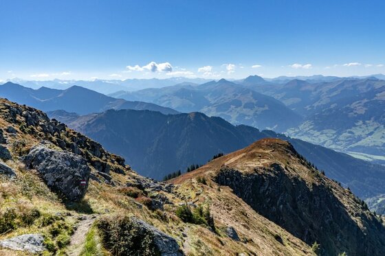 Südberge im Herbst Blick von einem felsigen Bergpfad auf eine weite Gebirgslandschaft unter blauem Himmel.