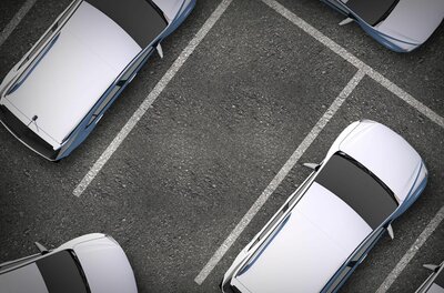 Draufsicht auf einen asphaltierten Parkplatz mit weißen Markierungen und geparkten Autos.