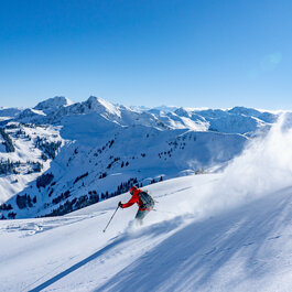 Im Skigebiet Kitzbühel fährt ein Skifahrer in roter Kleidung mit Schwung durch frischen Pulverschnee in den Bergen.
