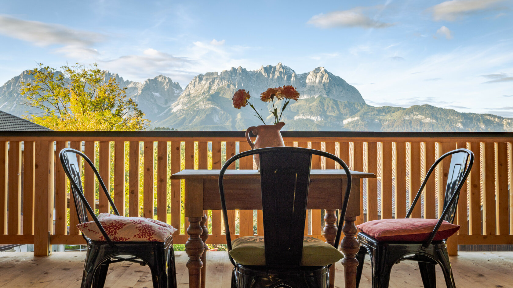 Der Blick von einem Holz-Balkon in Kitzbühel auf das Bergmassiv des Wilden Kaisers, mit einem Tisch und Stühlen, die zum Entspannen einladen.