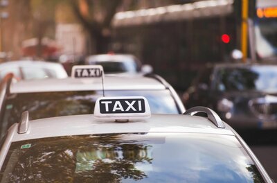 Several taxis are parked on a city street. The vehicles have a bright taxi sign on the roof.