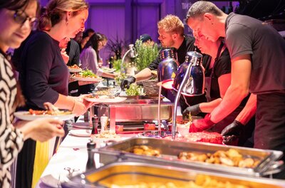 A buffet with various dishes is presented by several people. Guests choose from a variety of foods and enjoy the meal in a festive atmosphere.