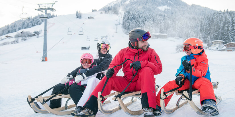 Eine fröhliche Gruppe von vier Personen sitzt auf Schlitten im Schnee, umgeben von einer malerischen Winterlandschaft.