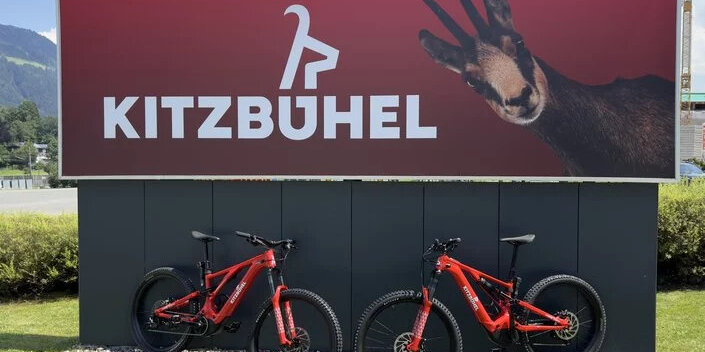 Zwei rote E-Bikes stehen vor einem großen Kitzbühel-Schild mit einem Bild einer Gämse im Hintergrund.