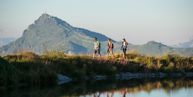 3 Personen, die neben einem See spazieren gehen