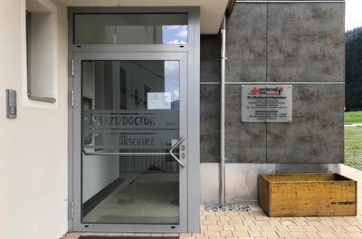 An entrance to a doctor's practice with a modern glass door. Next to the door, there is a sign.