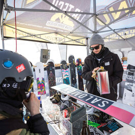 Skigebiet Kitzbühel, Snowboard Testday, Snowboarder bereitet sein Board im Zelt vor, Besucher schaut zu.