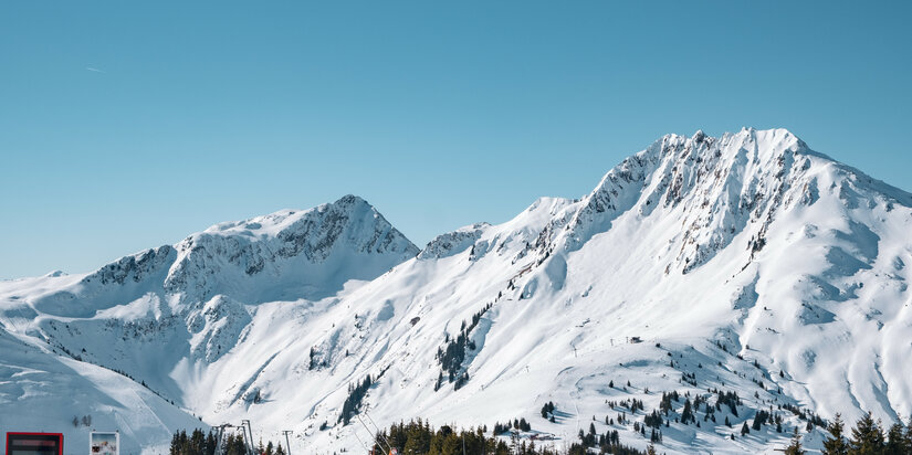 Am Kleinen Rettenstein im Skigebiet Kitzbühel erheben sich schneebedeckte Berge unter strahlend blauem Himmel.