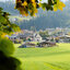 Blick auf ein Dorf in der Region Kitzbühel mit Kirche, umgeben von Herbstfarben und Hügeln.