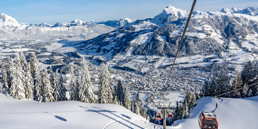Eine Seilbahn schwebt über schneebedeckte Berge, während die Aussicht auf das Tal und die Stadt im Hintergrund beeindruckt.