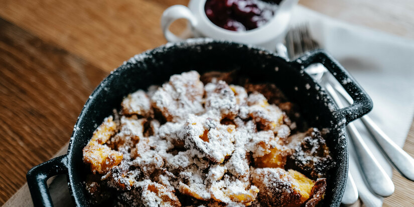 Kaiserschmarren, Skigebiet Kitzbühel, in Pfanne mit Puderzucker auf Holzbrett serviert.
