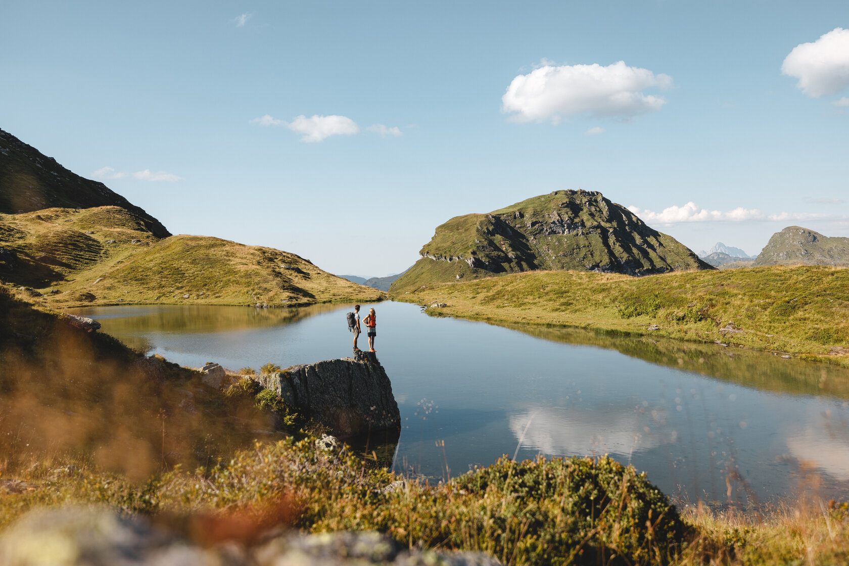 Ein Bergsee umgeben von Gras mit einem Gipfel im Hintergrund