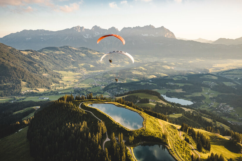 Zwei Paraglider schweben über die Berglandschaft in Kitzbühel bei Sonnenuntergang.