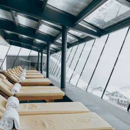 Ein lichtdurchfluteter Wellnessraum mit Liegen und Handtüchern, der eine ruhige Atmosphäre und einen Blick auf die verschneite Natur bietet.