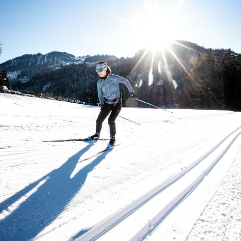 Beim Langlauf in Kitzbühel gleitet eine Langläuferin über verschneite Landschaft im strahlenden Sonnenlicht.