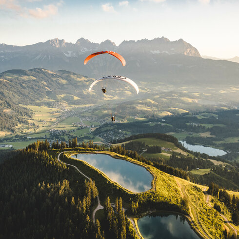 Zwei Paraglider schweben über die Berglandschaft in Kitzbühel bei Sonnenuntergang.